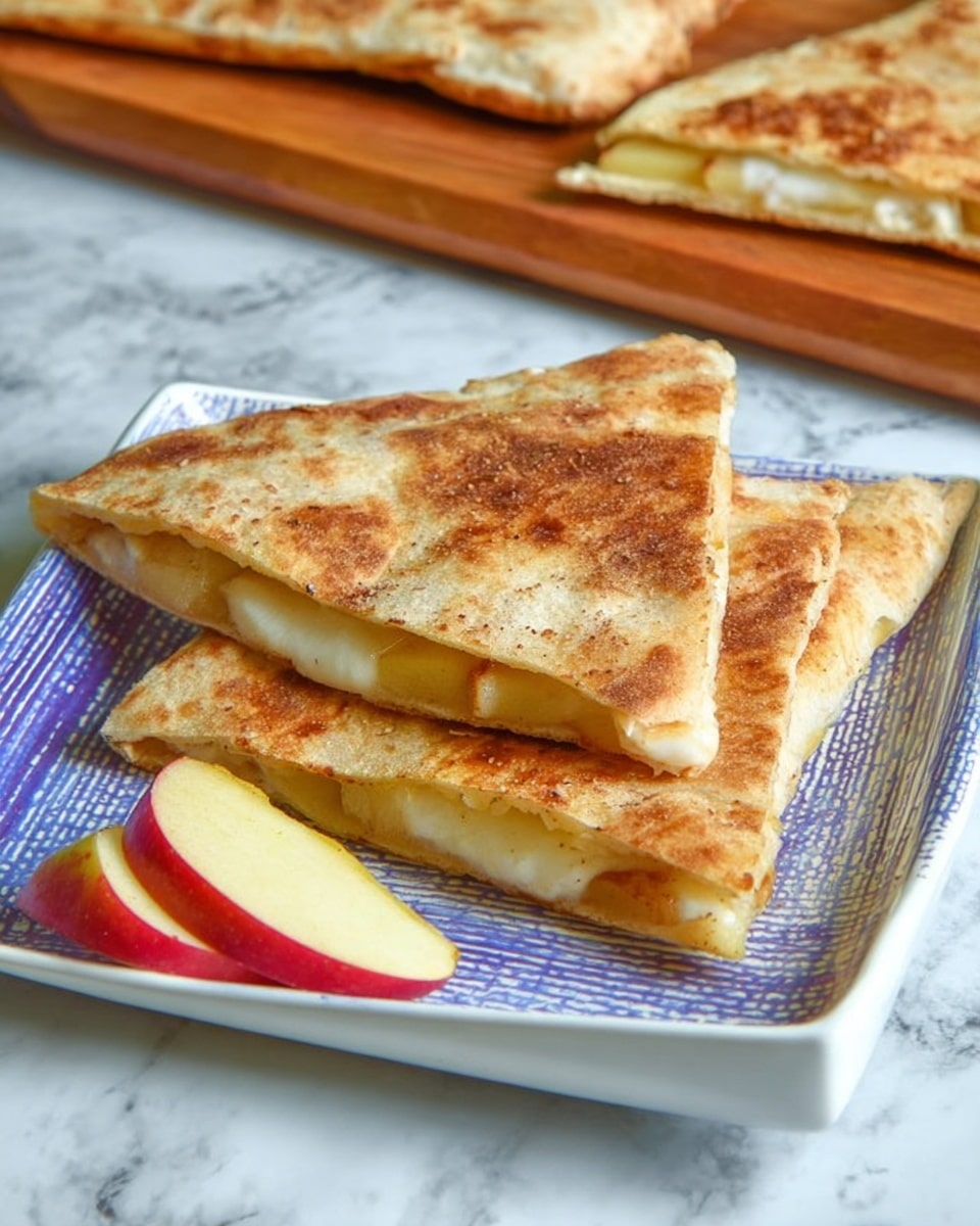 Two triangular pieces of toasted flatbread are stacked on a white square plate, each showing a golden-brown crispy surface with a slightly rough texture. Inside, thin slices of pale yellow apple are visible along with a layer of white melted filling, creating a soft contrast to the crispy outer layer. Two thin apple slices with red skin are placed beside the flatbreads on the plate. The plate is set on a white marbled surface, and in the background, a wooden board holds more pieces of flatbread. Photo taken with an iphone --ar 4:5 --v 7