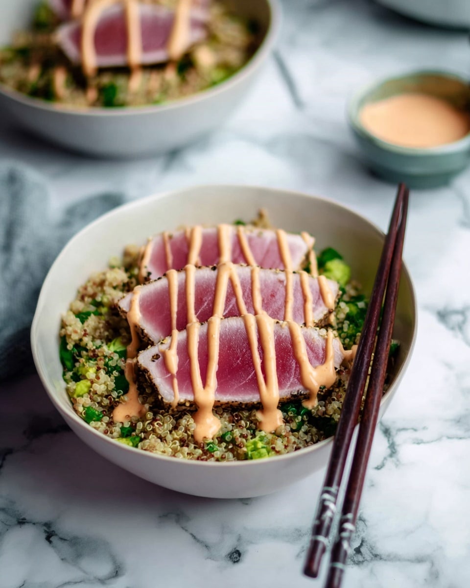The image shows a white bowl filled with three thick slices of pink, lightly seared tuna arranged neatly on top. Below the tuna lies a layer of mixed quinoa and chopped green vegetables with a grainy texture. Light orange sauce is drizzled in stripes over the tuna slices. A pair of dark wooden chopsticks rests against the side of the bowl. The bowl sits on a white marbled surface. In the blurry background, there is another similar bowl and a small cup with more sauce. photo taken with an iphone --ar 4:5 --v 7