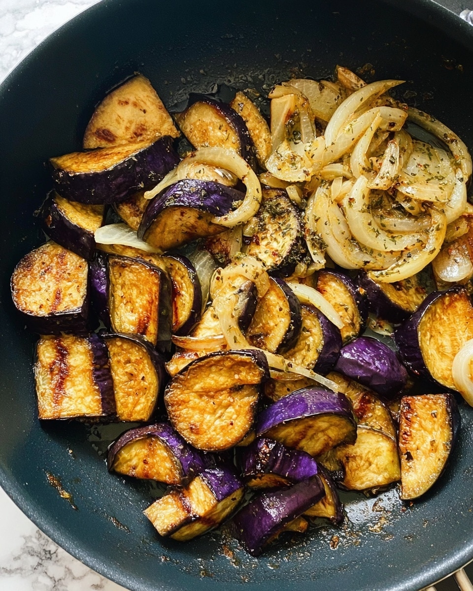 The image shows a black pan filled with cooked eggplant pieces and sliced onions. The eggplant pieces are in different sizes, with a mix of deep purple skin and golden brown cooked surfaces, showing a slightly shiny texture from the oil. The onions are light yellow with a soft, slightly translucent look, sitting mostly on one side of the pan. The whole dish has a glistening, cooked appearance with some small seasoning bits scattered over the vegetables. The background surface is a white marbled texture. photo taken with an iphone --ar 4:5 --v 7
