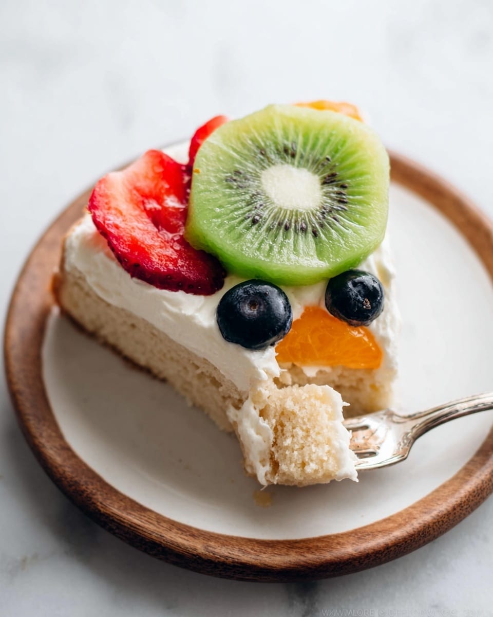 A slice of soft, light-colored cake sits on a round white plate with a smooth texture. On top of the cake is a thick layer of white cream. The cream is decorated with bright fruit slices: two red strawberry slices near the top, one large green kiwi slice in the center, and two small dark blue blueberries. A silver fork holds a bite-sized piece of cake and cream with an orange fruit piece near the plate. The plate is on a white marbled surface. Photo taken with an iphone --ar 4:5 --v 7