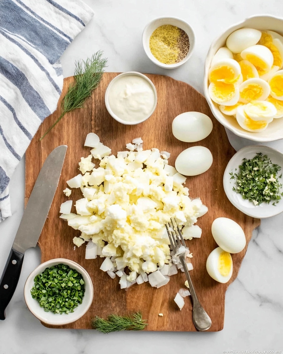 A wooden board on a white marbled surface holds chopped egg whites piled in the center with some halved egg whites around it. To the top right of the chopped eggs is a white bowl filled with yellow sliced egg yolks and a fork resting inside. Near the top center of the board is a small white bowl with a creamy white sauce, with a small sprig of green dill next to the board on the left. Surrounding the board are four small white bowls containing finely chopped green herbs, a mix of salt and pepper, yellow mustard, and more green herbs. A knife with a black handle rests on the left side of the board, and a striped white and blue cloth is partially visible in the top left corner. Photo taken with an iphone --ar 4:5 --v 7
