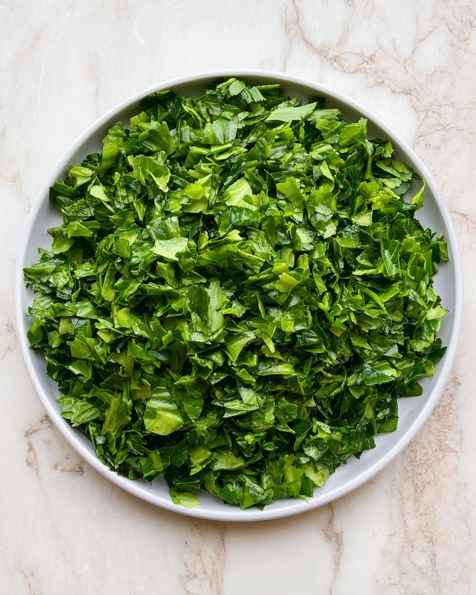A round white plate filled completely with finely chopped leafy greens that are bright green and fresh. The chopped pieces vary in size and texture, with some showing crisp edges and others slightly wilted, spread evenly across the plate's surface. The plate rests on a white marbled texture background, giving a clean and fresh look. photo taken with an iphone --ar 4:5 --v 7