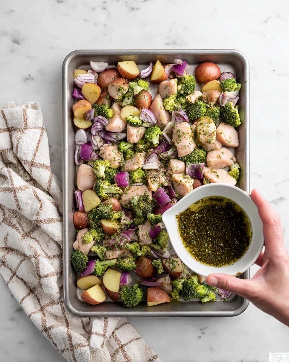 A silver baking tray holds a mix of raw chicken pieces, small red potatoes cut in halves, broccoli florets, and chunks of purple onion, all spread evenly across the bottom. Above the tray, a woman's hand holds a white bowl tilted downward, pouring a dark green herb mix with oil onto the ingredients. To the left of the tray, a beige and white checkered cloth rests on a white marbled surface. The colors in the mix show a contrast of light pink chicken, bright green broccoli, deep purple onions, and red potatoes. photo taken with an iphone --ar 4:5 --v 7