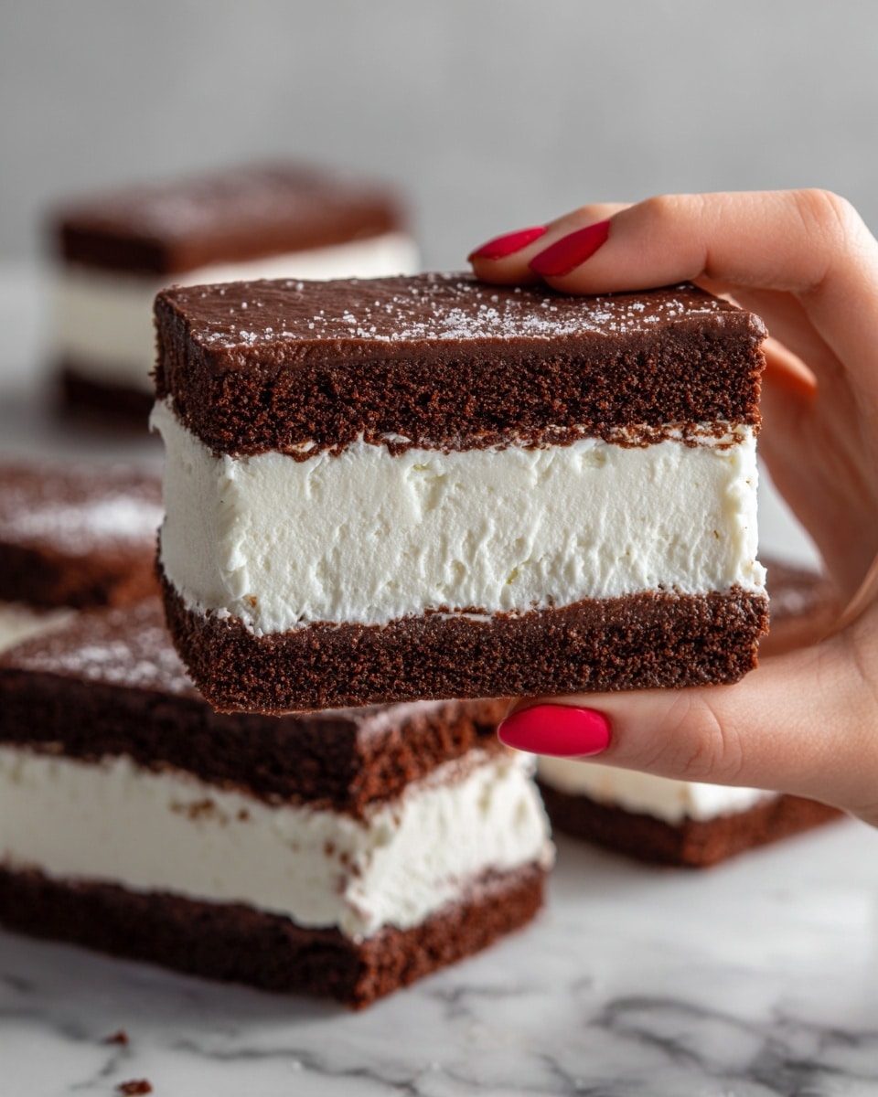 A close-up of a woman's hand holding a rectangular ice cream sandwich composed of two thick, dark brown chocolate cake layers on the top and bottom, with a thick, creamy white ice cream layer in the center. The texture of the chocolate cake appears soft and slightly crumbly, while the ice cream is smooth and dense. In the background, four more identical ice cream sandwiches are placed side by side on a white marbled surface. The woman's nails are painted red, adding a bright contrast to the dark and light colors of the dessert. photo taken with an iphone --ar 4:5 --v 7