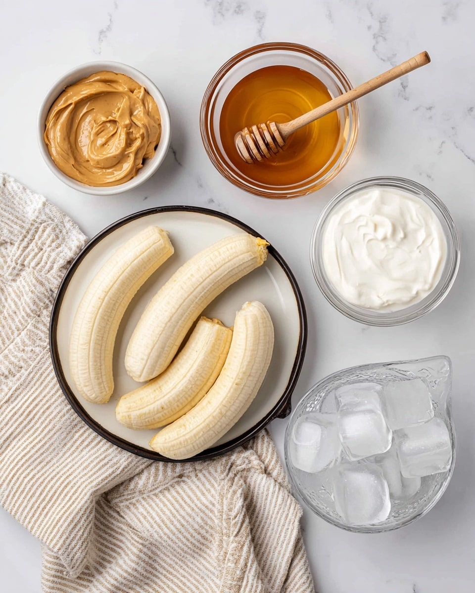 The image shows six frozen peeled bananas arranged on a white plate with a dark rim, placed on a white marbled surface. Around the plate are several small white bowls and a clear glass measuring cup: one bowl holds smooth peanut butter with a creamy texture, another has honey with a honey dipper resting inside, one bowl contains thick white yogurt, and a clear bowl filled with clear ice cubes. A beige kitchen towel with white stripes is laid beside the bowls. photo taken with an iphone --ar 4:5 --v 7