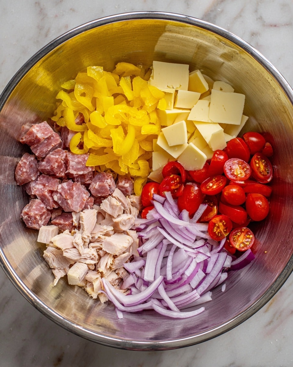 There is a large metal bowl on a white marbled surface filled with six separate layers of ingredients. At the top left are bright yellow chopped pickled peppers with a soft texture. Next to it on the top right are pale yellow square slices of cheese stacked in a pile. Below the peppers on the middle left is a group of thin, small pieces of cured meat with a dark pink color and some white fat marbling. To the center right, cherry tomatoes are halved and stacked with shiny red skins. At the bottom left, there are small cubes and flakes of light tan cooked turkey. Finally, on the bottom right, thin, rounded slices of purple-red onion with a white inside layer are arranged loosely. Photo taken with an iphone --ar 4:5 --v 7