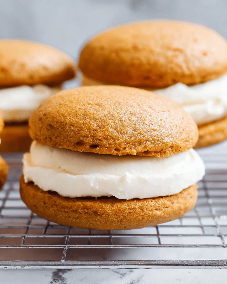The image shows a close-up of three small sandwich-like desserts stacked. Each dessert has two soft, rounded, light brown cake layers with a smooth texture, slightly uneven edges, and some tiny air pockets visible on the surface. Between the two cake layers is a thick layer of smooth, creamy white filling that looks fluffy and evenly spread. The desserts are placed on a metal cooling rack with a white marbled texture background softly blurred behind them. The focus is on the front dessert, showing its shape and texture clearly. photo taken with an iphone --ar 4:5 --v 7