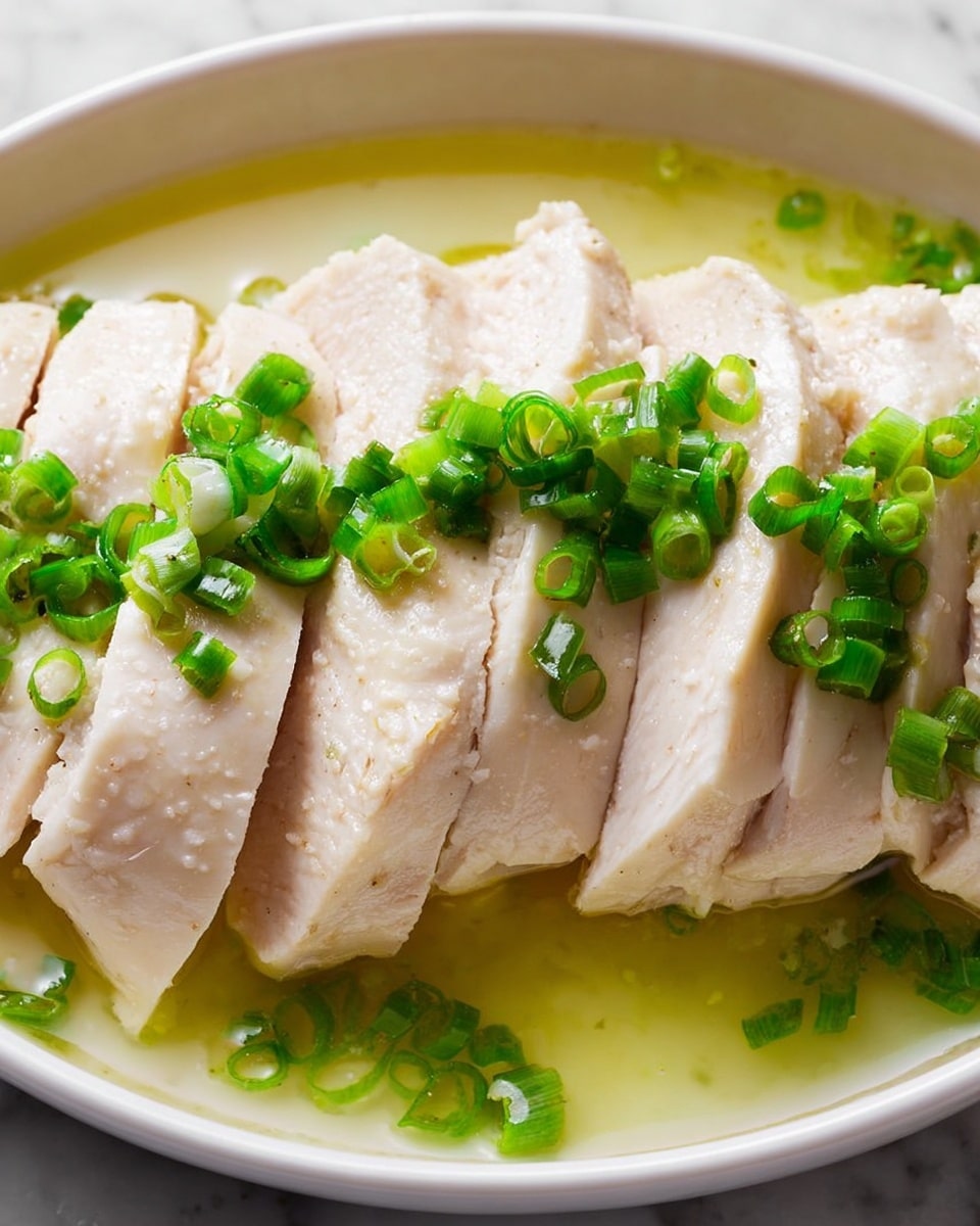 The image shows several slices of cooked white chicken arranged in a row on a white plate. The chicken has a smooth, moist texture with soft pale beige color. Bright green chopped scallions are sprinkled evenly over the top of the chicken slices, adding a fresh and vibrant contrast. The chicken sits in a thin layer of light yellow-green sauce or broth that pools around the base, giving the dish a glossy finish. The background is a white marbled texture. Photo taken with an iphone --ar 4:5 --v 7