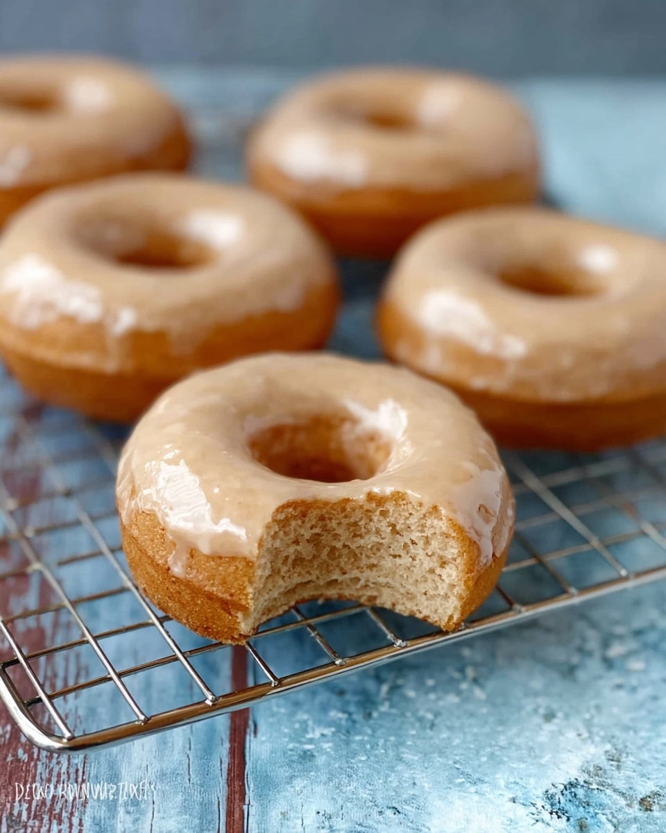 The image shows six round donuts placed on a metal cooling rack. Three of the donuts have a smooth, creamy beige glaze on top that looks slightly shiny and drips a little over the edges, while the other three are plain with a golden brown color and soft texture. The donuts have a small hole in the middle. The background is a white marbled texture. The overall look is simple and appetizing. photo taken with an iphone --ar 4:5 --v 7