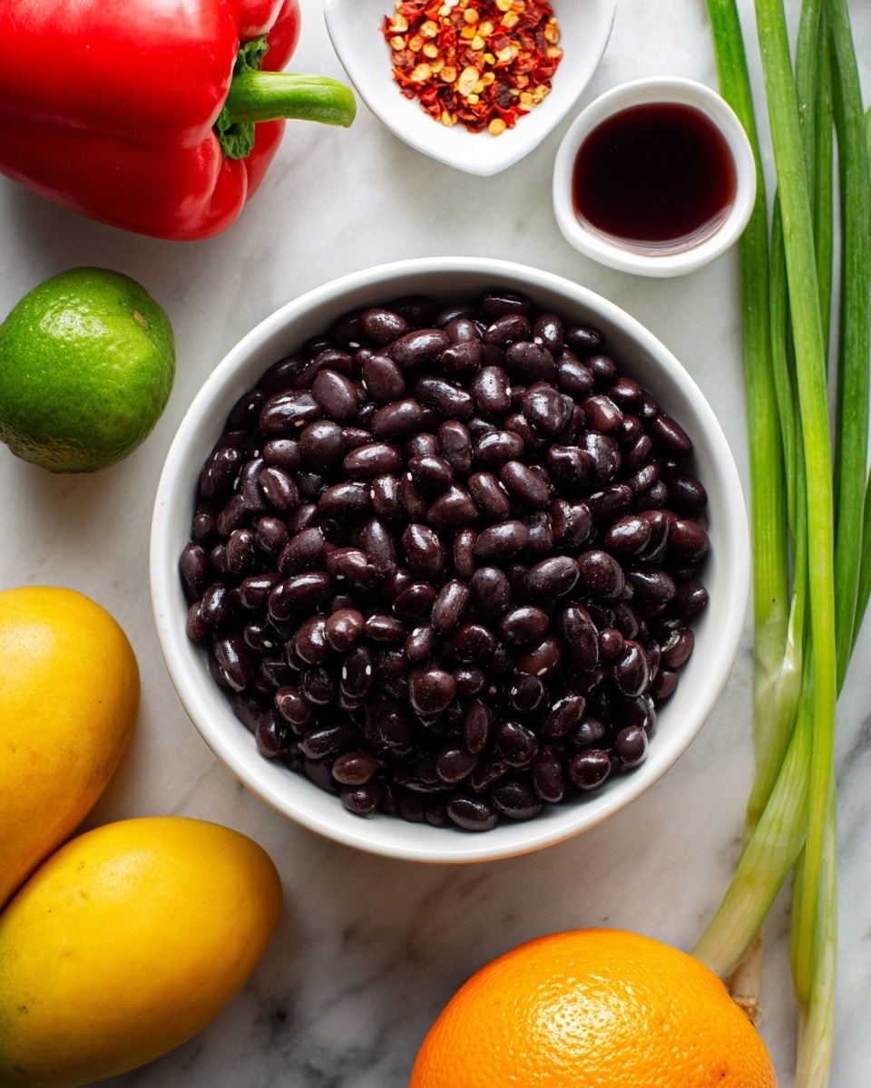 A white bowl filled with shiny black beans sits in the center on a white marbled surface. Surrounding the bowl are fresh ingredients: two yellow mangoes on the top right, three long green onions to the right, a whole bright orange orange on the bottom left, and a small green lime near the orange. To the left of the bowl, there is a whole red bell pepper and a small white dish with red pepper flakes. Above the bowl, a white container holds deep red wine vinegar, creating a colorful and fresh arrangement of ingredients. Photo taken with an iphone --ar 4:5 --v 7