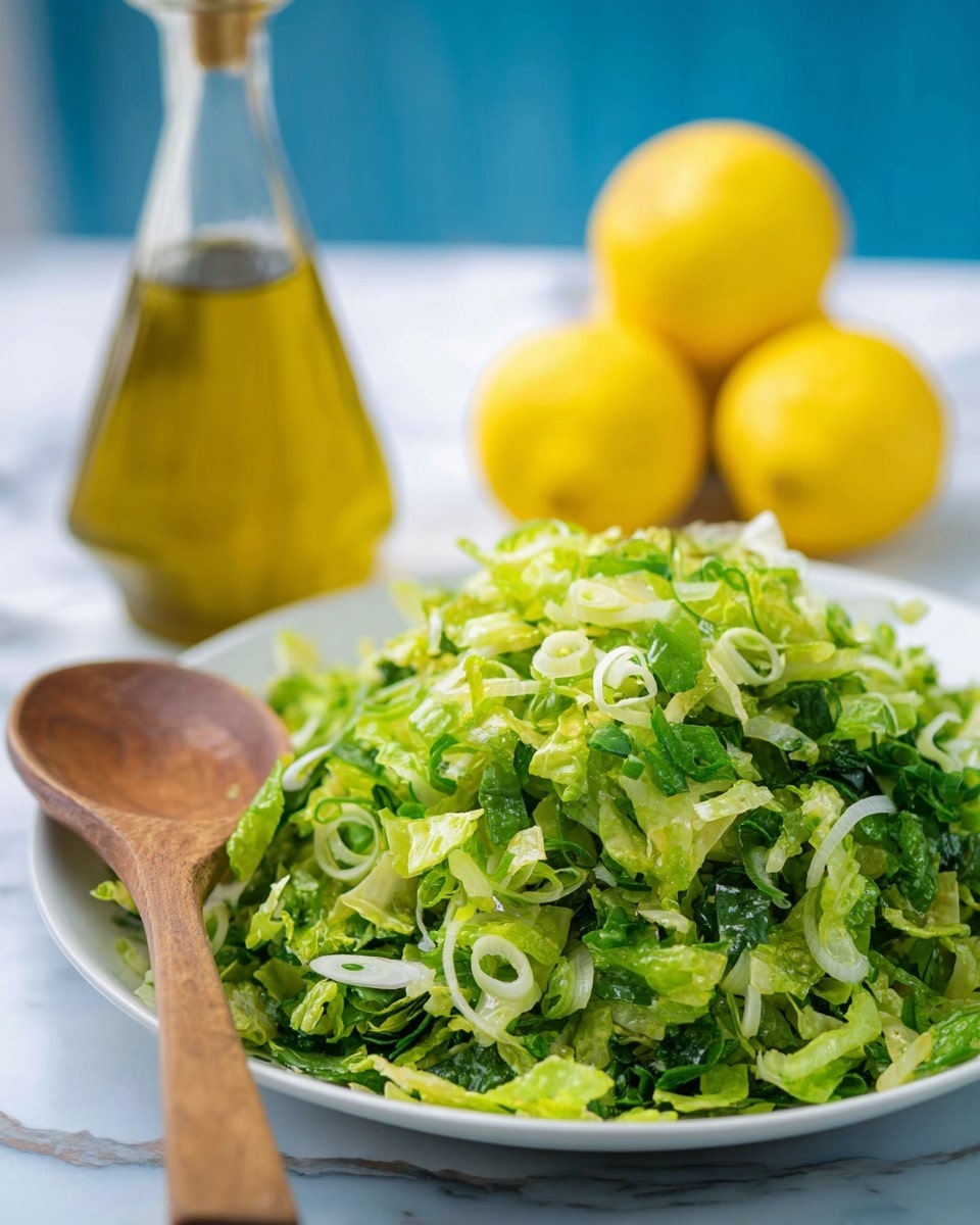 A white plate holds a mound of finely shredded bright green lettuce mixed with chopped light green scallions. The lettuce pile looks fresh and slightly shiny, showing texture from the small leaf pieces. A pair of wooden spoons rests across the front edge of the plate, one spoon lighter and the other darker in color. In the blurred background, a lemon cut in half and a green bottle sit on a blue surface. The whole scene is softly lit, highlighting the fresh vegetables. photo taken with an iphone --ar 4:5 --v 7