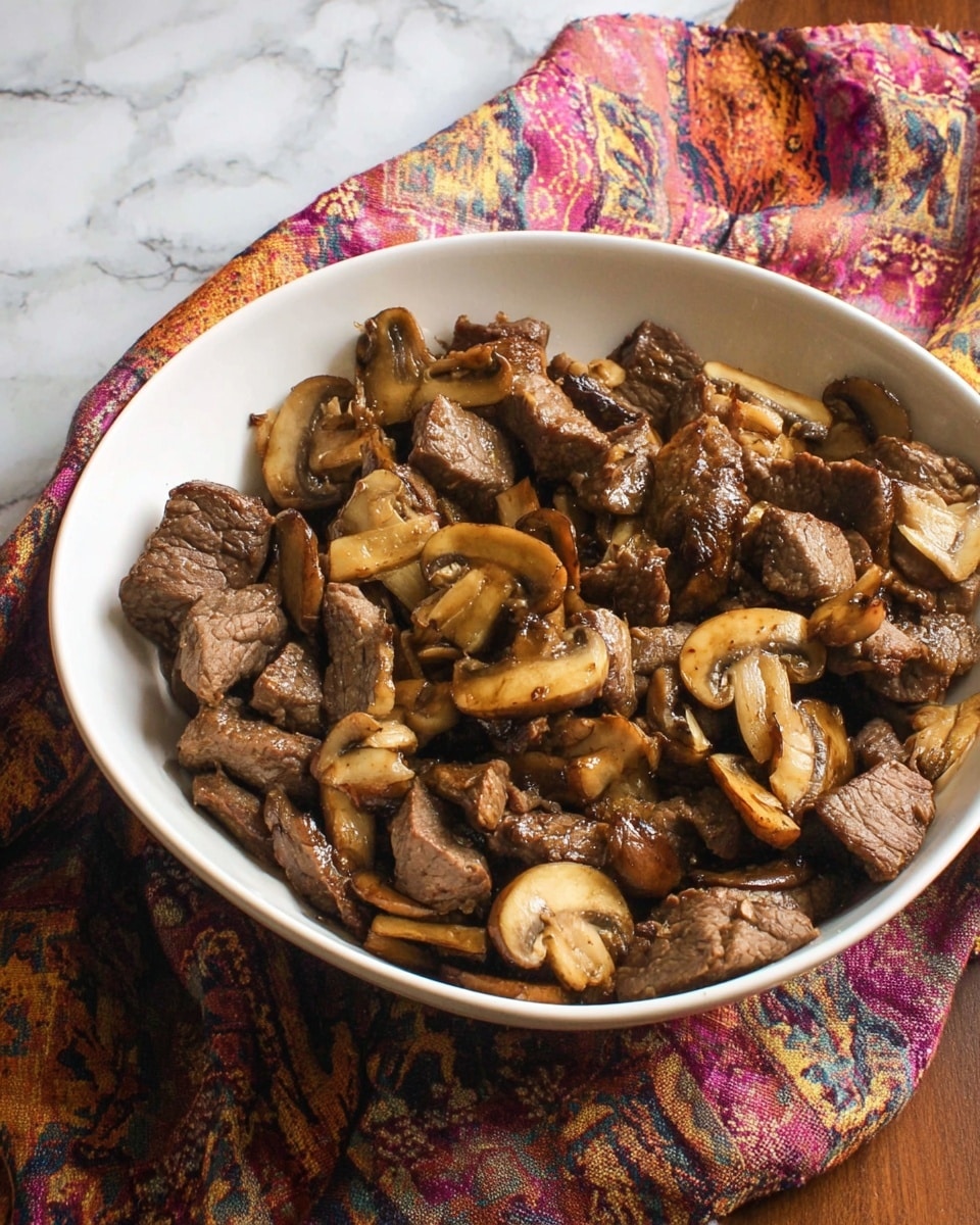 A white bowl filled with cooked pieces of brown beef and sliced mushrooms, showing a mix of tender meat chunks and golden-brown mushroom slices scattered evenly throughout. The dish looks juicy and slightly shiny, placed on a colorful cloth, all set on a white marbled surface. photo taken with an iphone --ar 4:5 --v 7