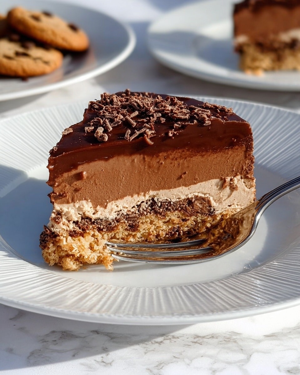A slice of layered chocolate dessert is placed on a white plate with a ridged edge, resting on a white marbled surface. The dessert has three main layers: the bottom layer is a light brown, crumbly cookie-like base with visible darker bits, the middle layer is a thick, creamy chocolate mousse with a smooth texture, and the top layer is a shiny, dark chocolate ganache sprinkled with fine chocolate shavings. A fork is gently pressed into the dessert from above, ready to take a bite. In the background, there are a few chocolate chip cookies and a blurred second plate with more dessert pieces. Photo taken with an iphone --ar 4:5 --v 7