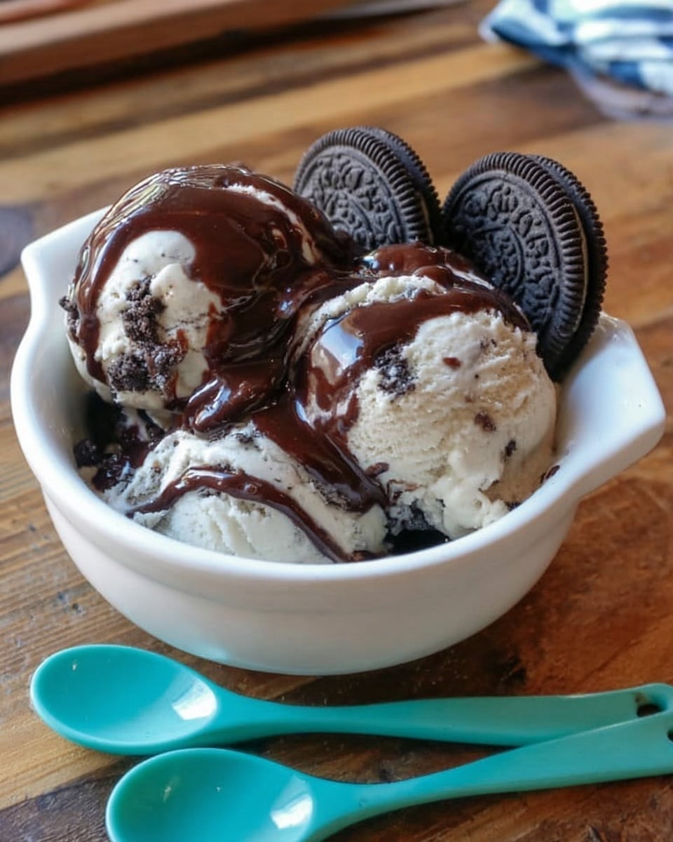 A white bowl with two handles filled with two scoops of cream-colored ice cream with dark cookie pieces mixed inside, topped with two whole sandwich cookies on one side. A woman's hand pours thick dark chocolate syrup from a glass jar directly onto the ice cream. In the background, there is a white marbled surface with a silver baking tray filled with similar ice cream and cookies, and some loose cookies nearby. The setting has a cozy, homemade feel with soft natural light. photo taken with an iphone --ar 4:5 --v 7