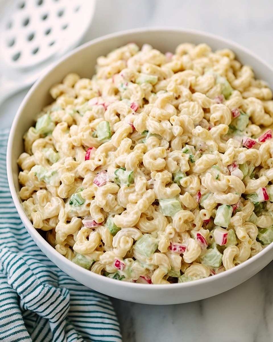 A close-up of a bowl filled with creamy macaroni salad, showing three main layers of small elbow pasta in pale yellow mixed with tiny pieces of pale green celery and light red onion bits, all coated in a smooth, creamy white dressing. The macaroni sits inside a white bowl with a white spoon lifting a portion from the bowl. The bowl is placed on a white marbled surface beside a teal cloth and a white cloth with blue stripes, creating a soft and inviting background. photo taken with an iphone --ar 4:5 --v 7