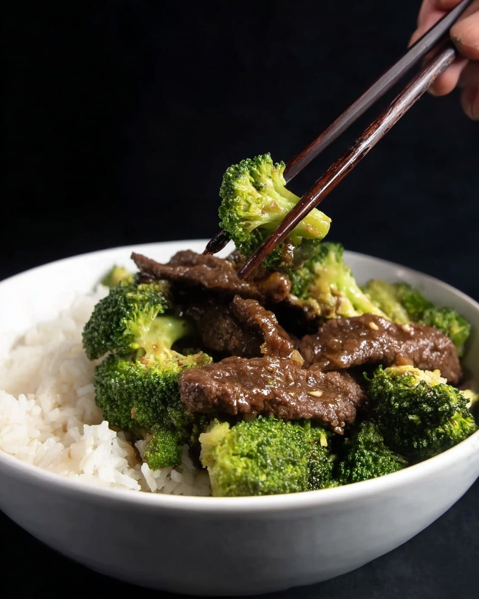 A white bowl filled with three main layers: at the bottom, there is a layer of white rice with a soft, slightly fluffy texture; on top of the rice, there are bright green broccoli florets with a firm, textured surface; resting on the broccoli, there are several pieces of dark brown beef strips glazed with a glossy sauce. A woman's hand holding dark wooden chopsticks is lifting one piece of the beef in the foreground. All of this is set against a black background. photo taken with an iphone --ar 4:5 --v 7