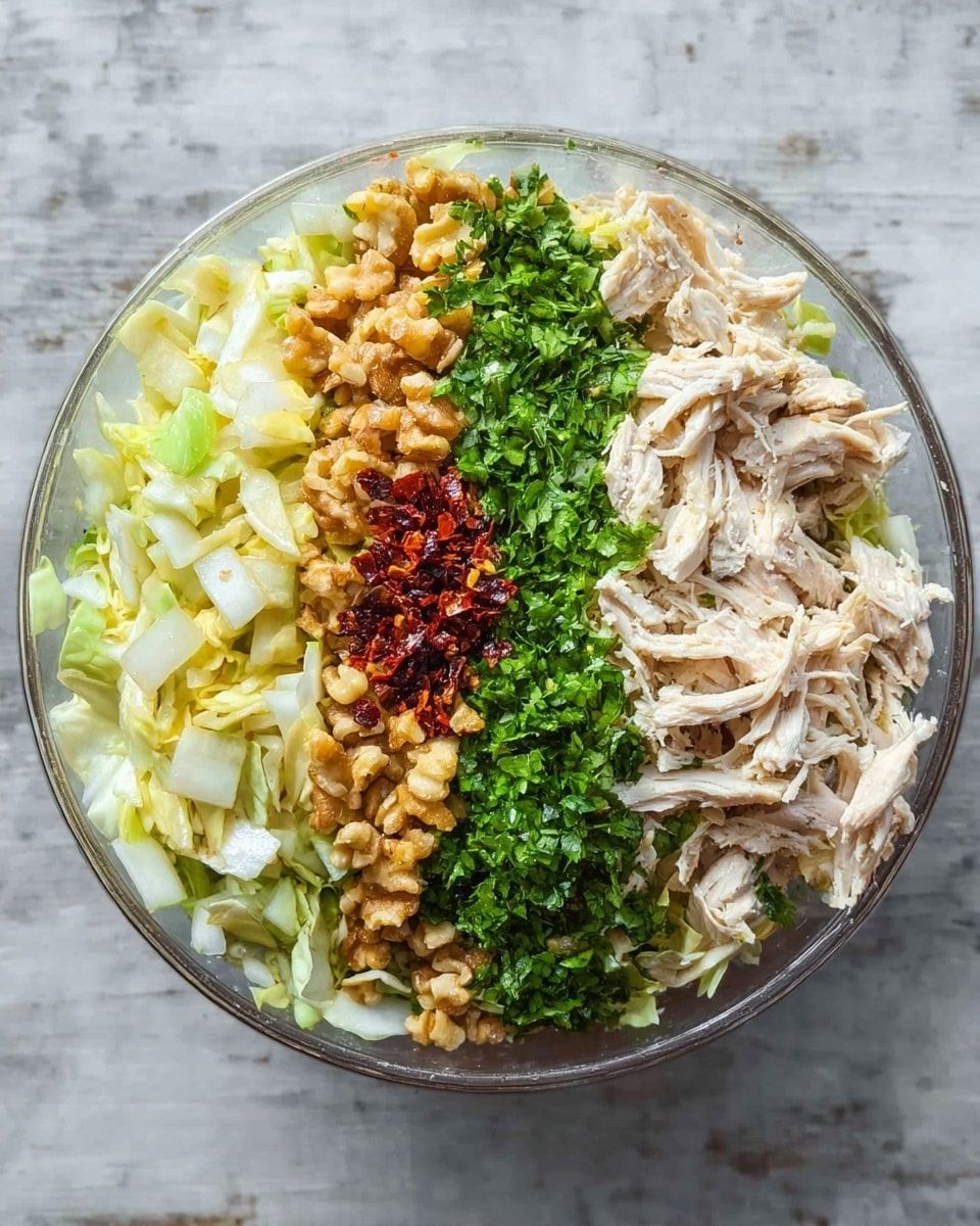 A clear white bowl holds a colorful, layered salad with five main sections, each occupying a neat vertical strip. On the left side, diced light yellow cabbage pieces form the first layer, followed by a pile of golden-brown crushed walnuts next to it. A small amount of dark red dried chili flakes is placed between the walnuts and a thick middle layer of bright green chopped herbs that runs vertically through the center. On the right side of the herbs, shredded light beige chicken fills the remaining space with some green herbs sprinkled on top. The bowl is placed on a white marbled textured surface. photo taken with an iphone --ar 4:5 --v 7