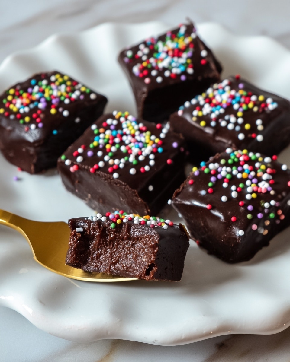 A rectangular chocolate dessert with a glossy dark chocolate top layer is placed on parchment paper on a wooden board over a white marbled surface. The dessert is topped with small, colorful round sprinkles scattered evenly across its surface. It is cut into six square pieces, with one piece slightly pulled away from the group, showing a thick texture with two visible layers: a solid dark chocolate top layer and a denser, fudgy bottom layer. Photo taken with an iphone --ar 4:5 --v 7