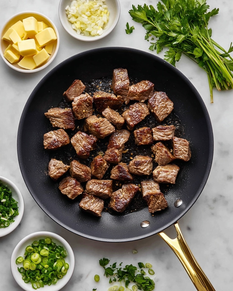 A black frying pan with a gold handle holds about 20 pieces of browned beef cubes evenly spread inside; the beef is a mix of medium brown colors with lightly charred edges showing a cooked texture. Around the pan on a white marbled surface are five small white bowls: one with yellow cubes of butter, one with finely chopped garlic, one with chopped fresh green herbs, and another with sliced green onions, with a few sprigs of fresh parsley scattered nearby. Photo taken with an iphone --ar 4:5 --v 7