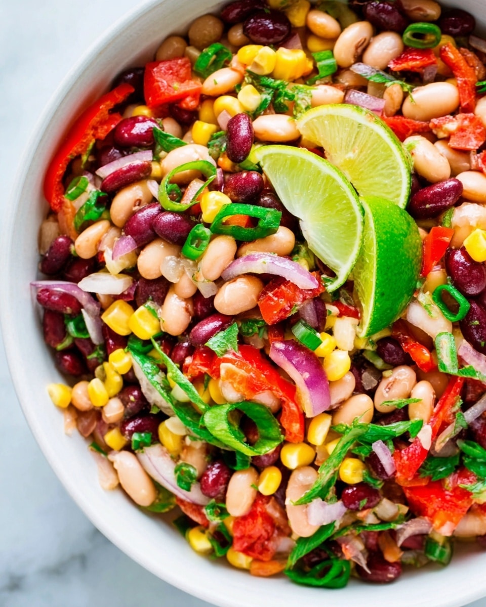 This image shows a colorful bean salad in a white bowl on a white marbled surface. The salad has multiple layers of beans including white, red, and black beans. There are small pieces of yellow corn, thin strips of red bell pepper, and slices of red onion mixed throughout. Bright green chopped scallions and a few green herbs are sprinkled on top. Two fresh lime wedges sit on top of the salad, adding a fresh contrast to the vibrant mixture. The textures range from soft beans to crunchy vegetables, all fresh and well-mixed. photo taken with an iphone --ar 4:5 --v 7