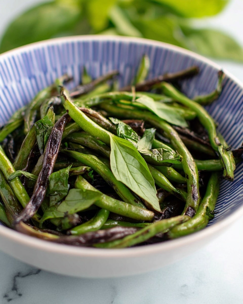 A bowl filled with green and purple long beans mixed with fresh green basil leaves. The beans are glossy and slightly charred, giving them a textured look with some spots darker than others. The white bowl has a blue striped pattern on the inside rim and sits on a white marbled surface. In the background, there are blurred green leaves providing a natural vibe. The overall image focuses closely on the beans, showing details of their colors and shapes. Photo taken with an iphone --ar 4:5 --v 7