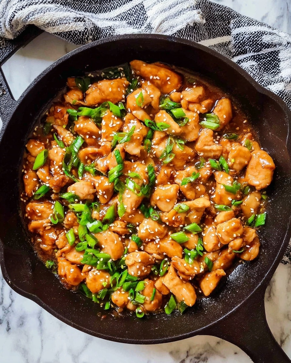A black cast iron pan filled with cooked pieces of chicken in a shiny brown sauce, mixed with bright green chopped spring onions and small white sesame seeds sprinkled on top, all resting on a white marbled surface with a black and white striped cloth nearby photo taken with an iphone --ar 4:5 --v 7