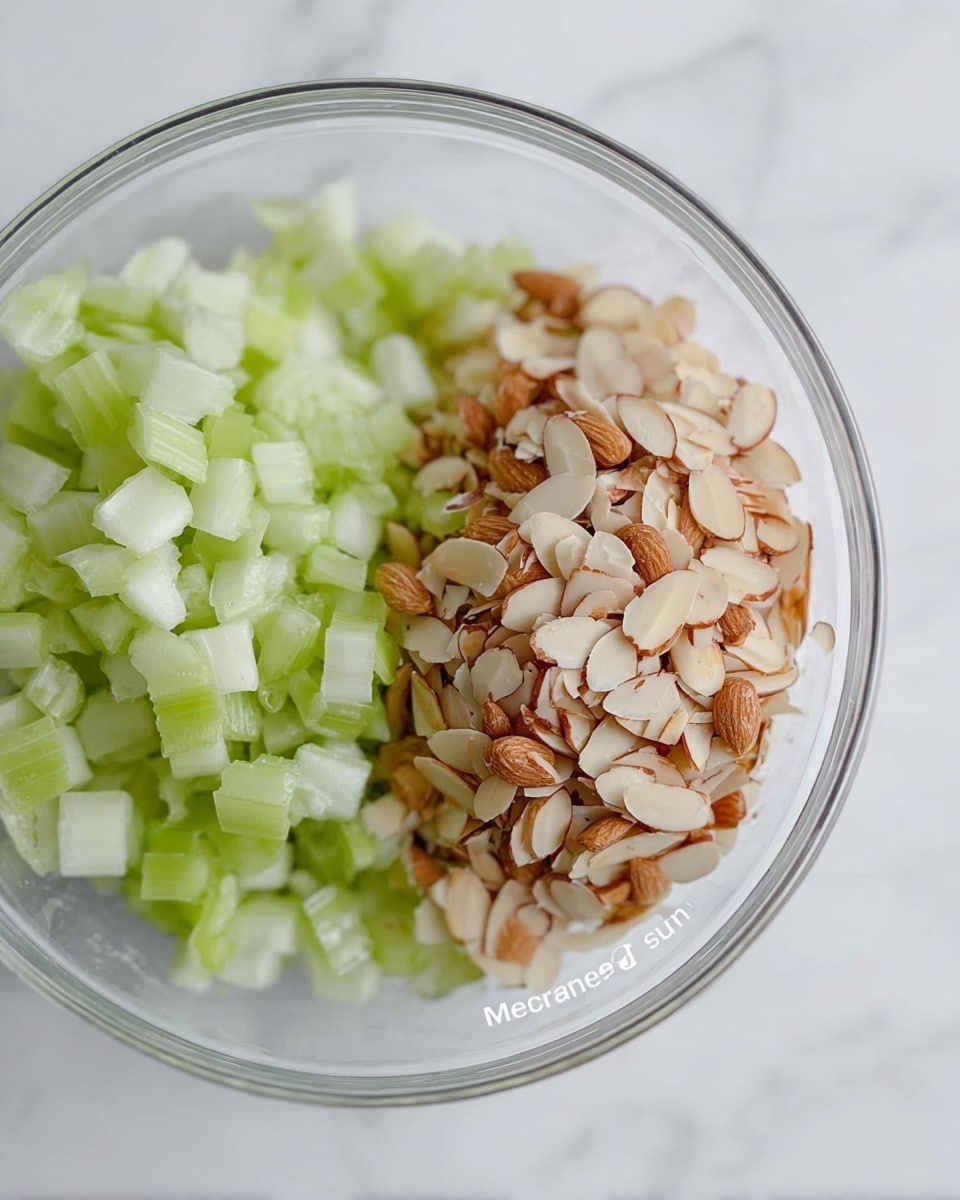 The image shows a clear glass bowl on a white marbled surface, filled with two ingredients layered side by side. On the left, there are small, light green celery pieces with a crunchy texture. On the right, there are thin, light tan almond slices with a slightly rough texture and bits of brown skin still attached. The bowl is viewed from above, allowing a clear view of the two ingredient piles. Photo taken with an iphone --ar 4:5 --v 7