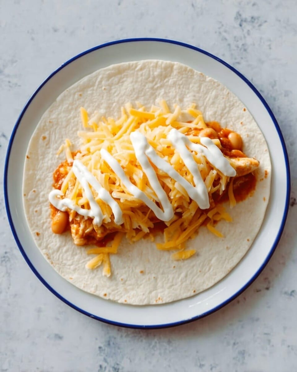The image shows a white tortilla laid flat on a white plate. On top of the tortilla in the center, there is a layer of chunky orange sauce with beans visible, covered by a layer of shredded orange-yellow cheese. On top of the cheese, there is a zigzag line of white sour cream. The plate is set against a white marbled surface. Photo taken with an iphone --ar 4:5 --v 7