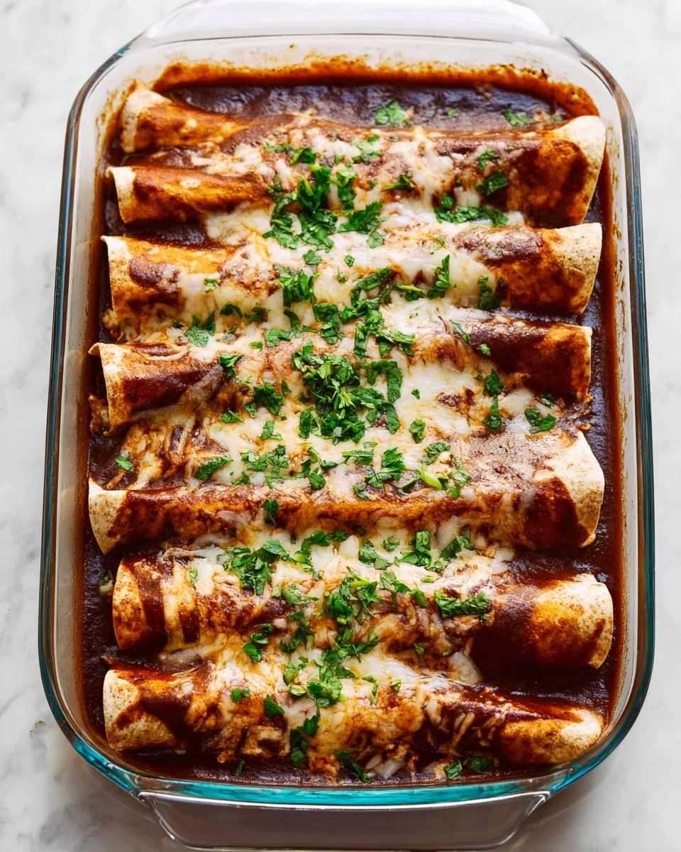 A clear glass tray holds six rolled enchiladas laid side by side, each topped with a thick layer of melted light beige cheese that is slightly browned in spots. Beneath the cheese is a rich, dark reddish-brown sauce that pools around the edges. The tortillas, visible at the ends and edges, are light brown and soft. Bright green chopped herbs are sprinkled generously over the top, adding a fresh contrast. The tray sits on a white marbled surface. photo taken with an iphone --ar 4:5 --v 7