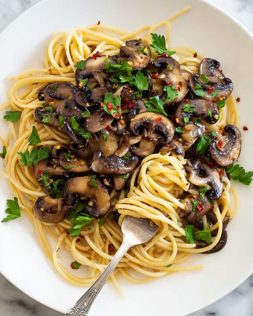 A white plate holds a serving of spaghetti pasta as the base layer, with a light yellow color and smooth texture, loosely piled in the center. On top of the pasta, there is a generous layer of sautéed dark brown sliced mushrooms with a shiny, slightly oily surface, scattered evenly over the noodles. Bright green parsley leaves are sprinkled on top, adding contrast with their fresh, leafy texture. Small red chili flakes are visible, scattered across the mushrooms and pasta, adding pops of red color. A silver fork is poking into the spaghetti near the center. The plate rests on a white marbled surface. Photo taken with an iphone --ar 4:5 --v 7