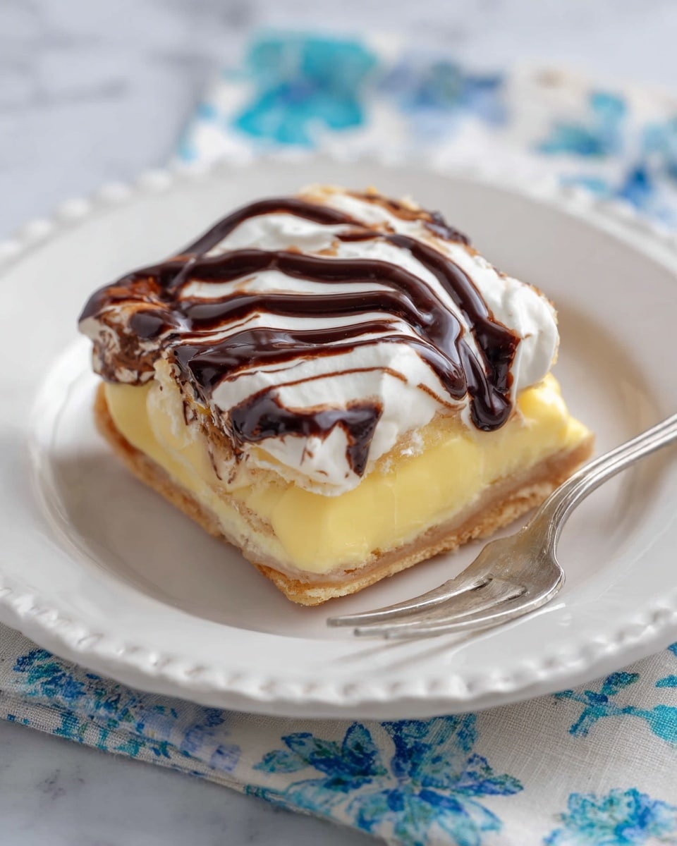 A square dessert with three visible layers sits on a white plate with ridged edges; the base is a light golden brown crust, topped by a thick pale yellow custard middle layer, and finished with a fluffy white layer of whipped cream that is swirled with dark chocolate syrup in irregular patterns. A small bite piece with all three layers is placed at the front on a silver fork. The plate is on a white marbled surface with a floral-patterned blue and white cloth partly visible underneath. photo taken with an iphone --ar 4:5 --v 7