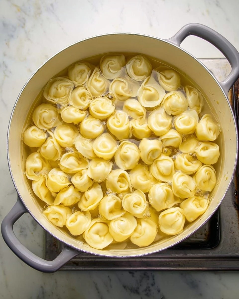 The image shows a large white pot filled with many small, folded dumplings floating in water on a stove. The dumplings are pale yellow with smooth, slightly shiny surfaces, arranged closely together and partially submerged in the clear broth. The pot has gray handles, and the background is a white marbled texture. photo taken with an iphone --ar 4:5 --v 7