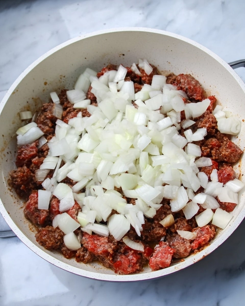 The image shows a white pan containing a mixture of two layers: the bottom layer is browned and partly cooked meat with a rich, slightly crispy texture, and the top layer is fresh diced white onions scattered evenly over the meat. The scene is set on a surface with a white marbled texture. photo taken with an iphone --ar 4:5 --v 7