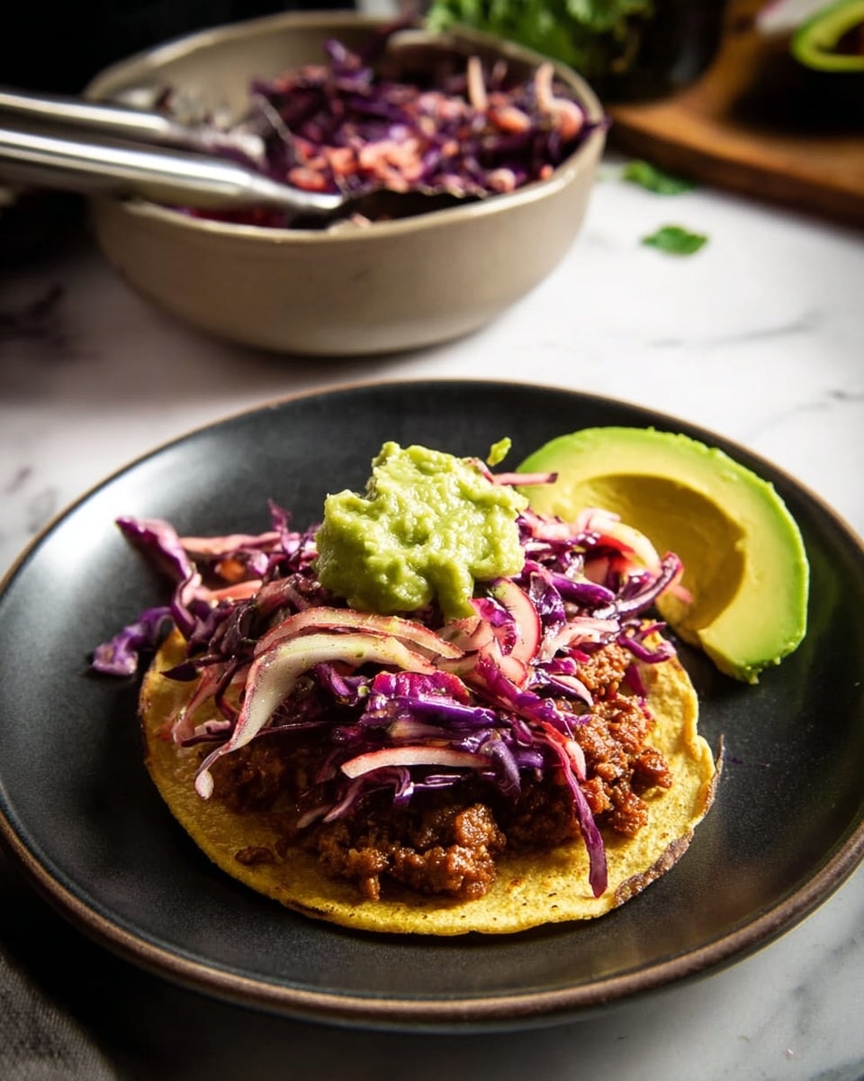 A single taco on a dark plate with a yellowish tortilla base, topped with a layer of ground meat that looks brown and crumbly. Above the meat is a mix of shredded purple cabbage and pinkish strips, giving a fresh, crunchy look. On top of the cabbage is a scoop of bright green guacamole, and beside the taco on the plate are two slices of soft, light green avocado. In the background, there is a bowl with more shredded cabbage and tongs, all set on a white marbled surface. photo taken with an iphone --ar 4:5 --v 7