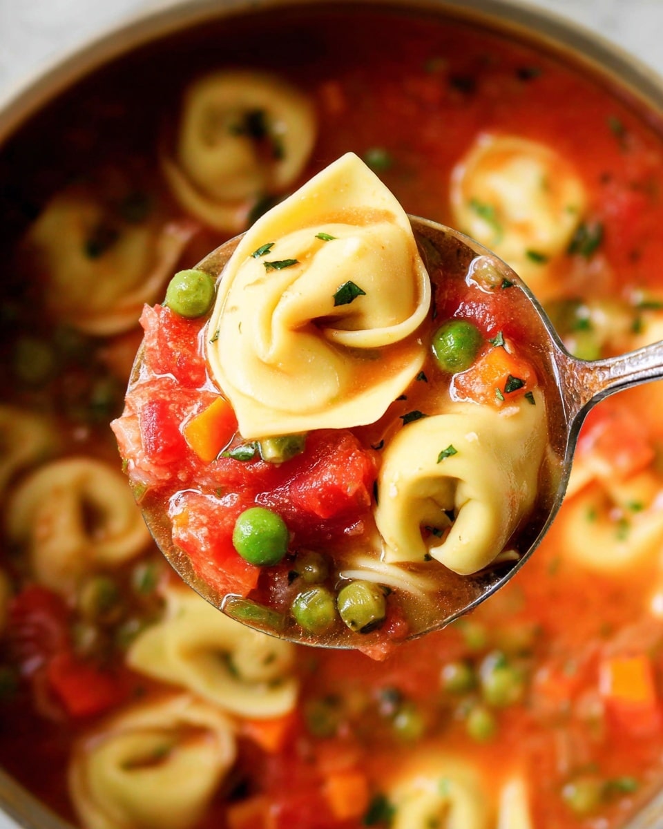 A close-up scoop of tortellini pasta in tomato broth held by a spoon, showing three main layers: the first layer has pale yellow tortellini pieces with smooth, folded texture; the second layer contains bright green peas and vibrant red and orange diced vegetables scattered evenly around the pasta; the third layer is a rich, chunky red tomato broth that fills and surrounds the tortellini and vegetables, all set on a white marbled surface background. photo taken with an iphone --ar 4:5 --v 7