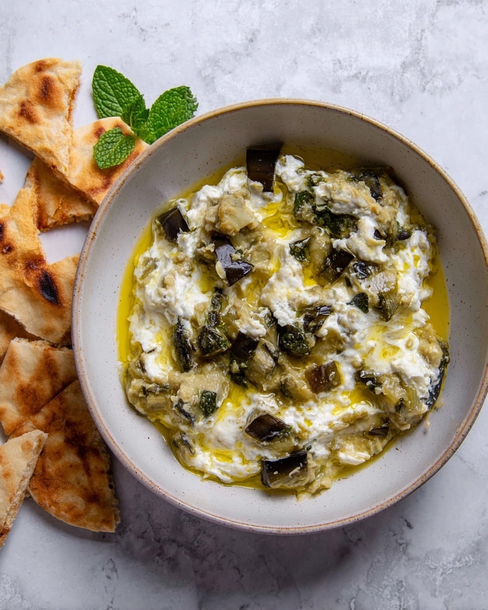 The dish shows a textured mix of soft, light green mashed vegetable pieces layered with dark green leafy bits spread unevenly in a shallow white bowl. Swirls of creamy white sauce are mixed in and patches of glossy yellow oil are drizzled on top, creating a shiny surface. The bowl sits on a white marbled surface with broken tan crackers and fresh green herbs as background accents. Photo taken with an iphone --ar 4:5 --v 7