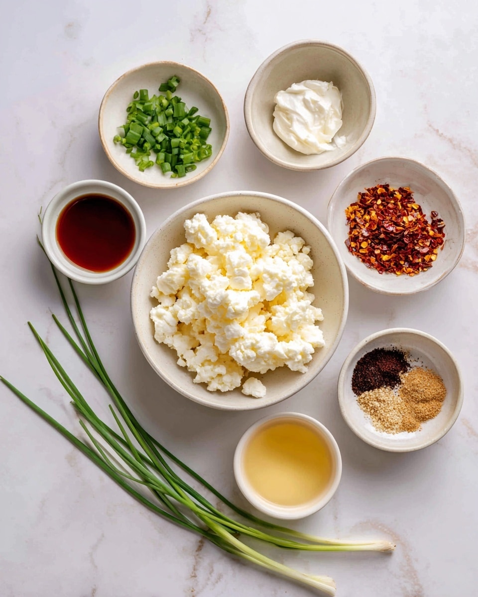 A top-down view of seven white bowls arranged on a white marbled texture, each holding different ingredients. The largest bowl in the center contains small, soft white curds with a creamy texture. Surrounding it are smaller bowls: one with chopped green chives, another with a dark reddish-brown liquid, one with a soft white cream, a bowl of crushed red chili flakes with orange and brown tones, a small bowl holding a pale yellow liquid, and a divided dish with light brown and black powdered spices. Fresh green chive stalks lay on the white marbled surface next to the bowls. The image has bright, soft lighting. Photo taken with an iphone --ar 4:5 --v 7