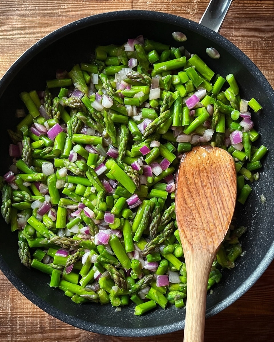 A black frying pan filled with chopped green asparagus and small pieces of purple and white onion being stirred by a wooden spoon resting inside the pan. The asparagus pieces are bright green with a fresh, slightly glossy texture, mixed evenly throughout with translucent diced onion. The pan sits on a wooden surface. photo taken with an iphone --ar 4:5 --v 7