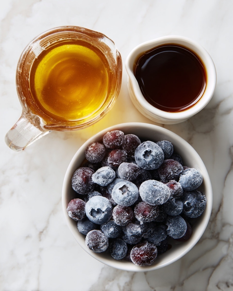 The image shows three main items placed on a white marbled surface. At the bottom center, there is a white bowl filled with frozen blueberries, covered with a layer of frost giving them a white powdery texture over the deep purple and blue berries. To the top left, there is a clear glass measuring jug containing golden amber apple juice, showing smooth liquid with a slightly reflective surface. To the top right, there is a small white ceramic jug filled with dark brown maple syrup, its surface smooth and shiny. The overall scene is bright and clean, with each item distinct and clearly visible. photo taken with an iphone --ar 4:5 --v 7