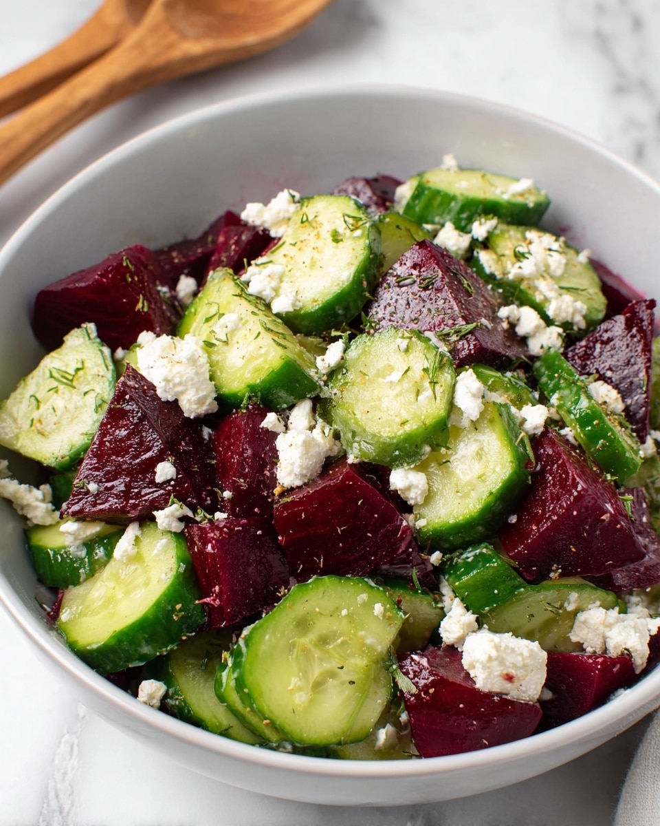 A white bowl filled with a fresh salad shows three main layers: the bottom layer is thick chunks of dark red beets with a smooth texture, the middle layer is bright green cucumber slices cut into half-moons with a crisp look, and on top are small crumbles of white cheese scattered evenly. The salad is lightly sprinkled with dried herbs adding fine green specks. The bowl sits on a white marbled surface with a wooden spoon partially visible in the background. photo taken with an iphone --ar 4:5 --v 7